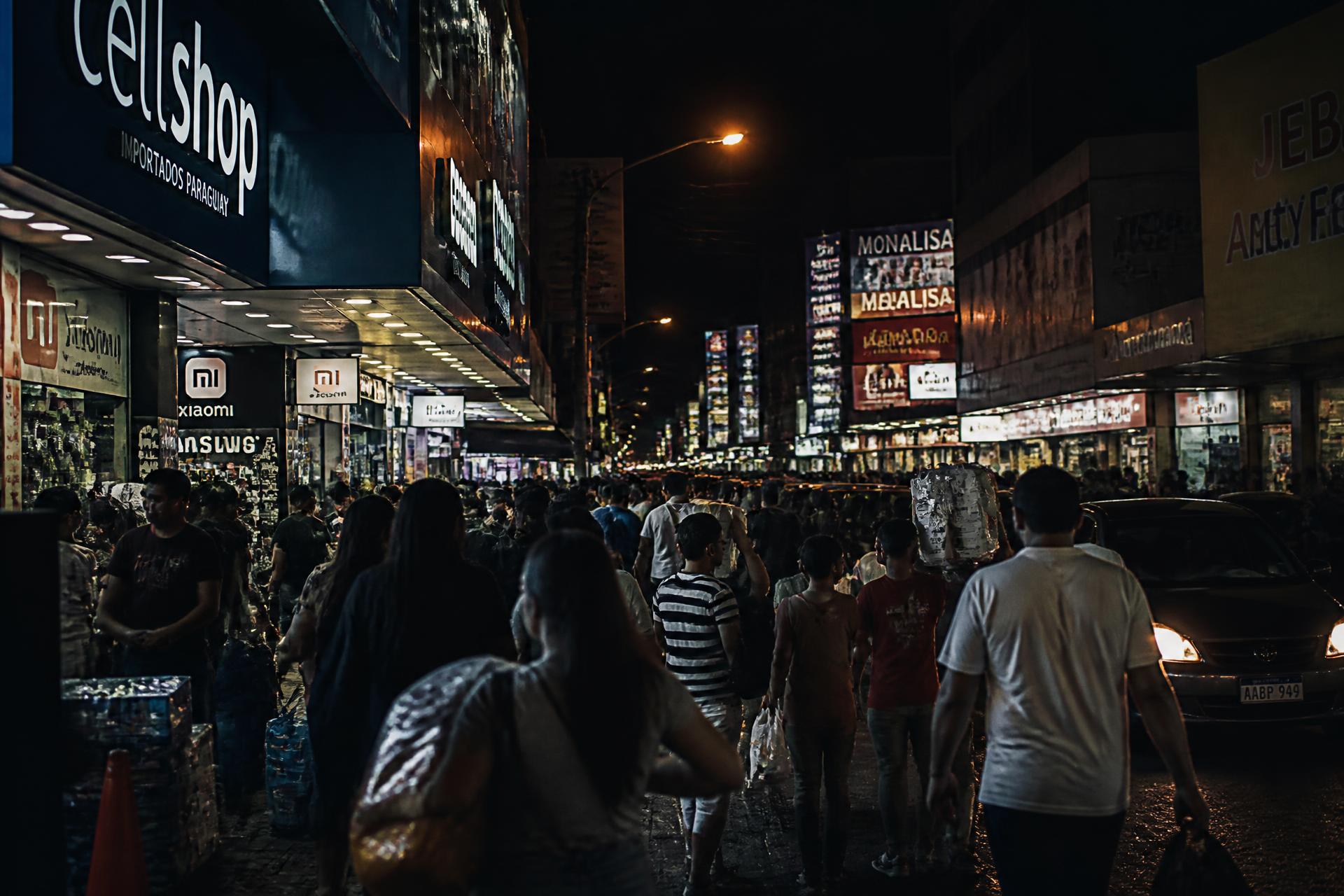 Centro comercial de Ciudad del Este à noite, com lojas de eletrônicos e movimento de compradores